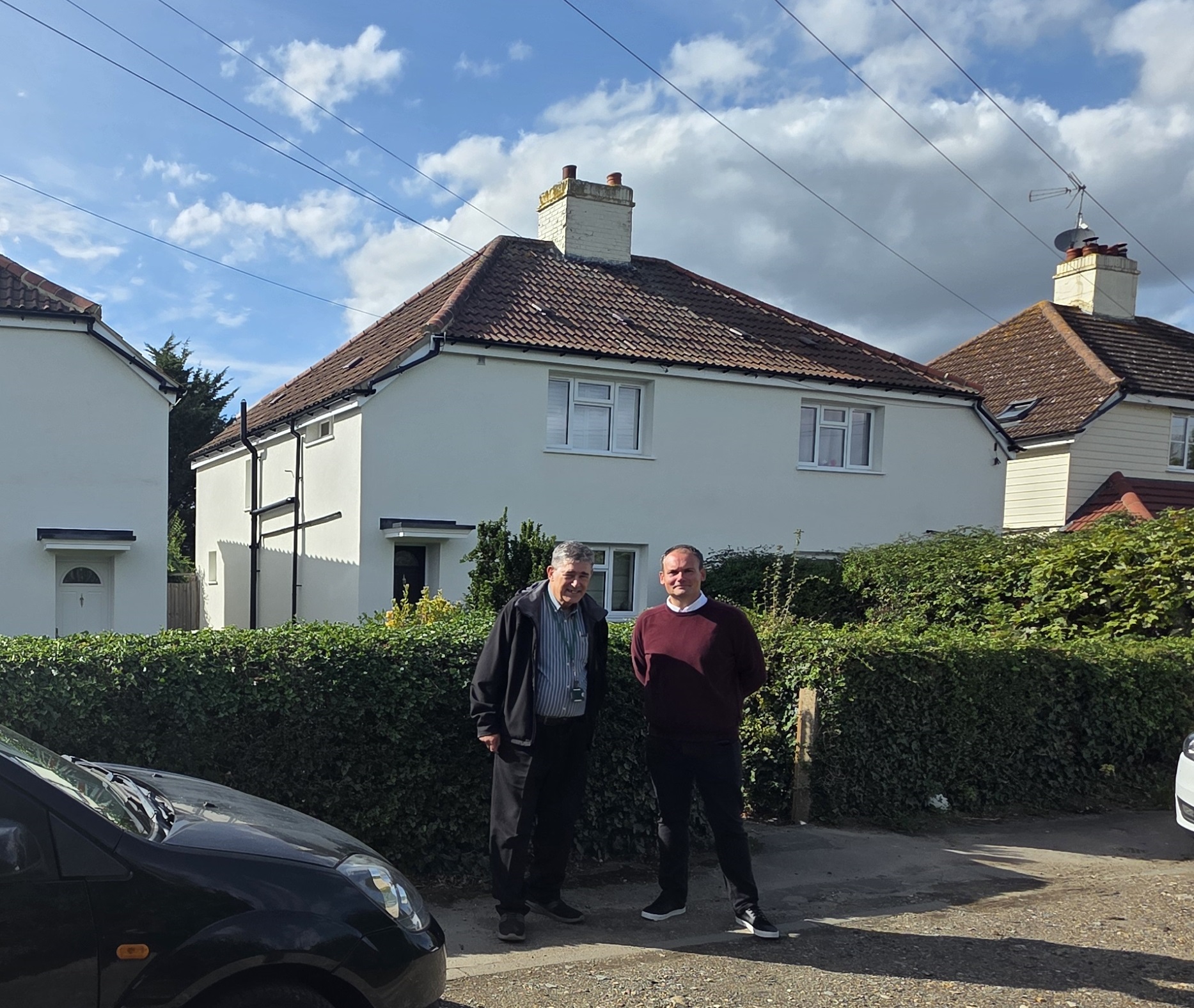 Image shows two men, smiling at the camera, in front of three semi-detached homes