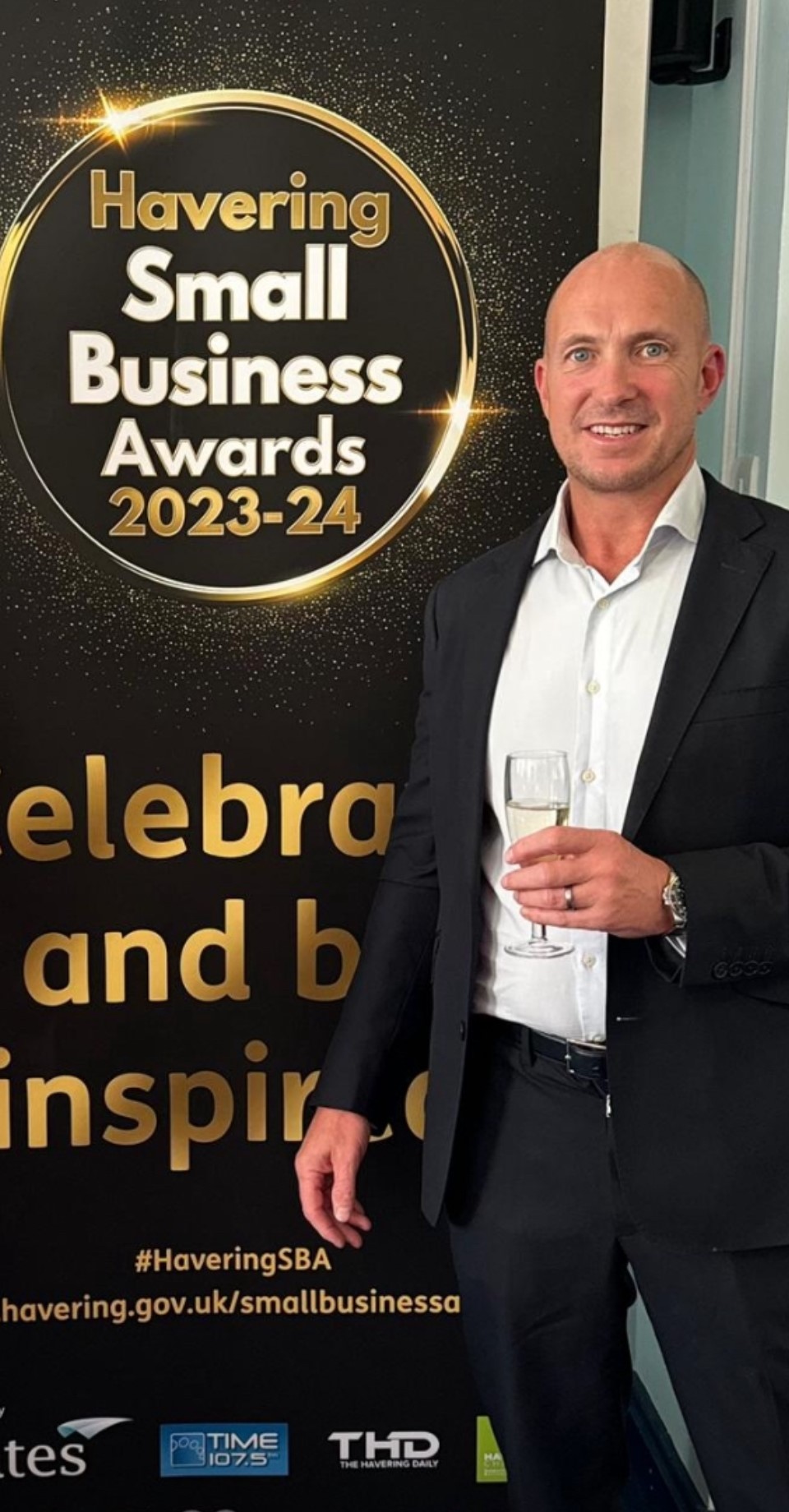 Image shows Paul Perfect smiling at the camera in front of a Small Business Awards banner